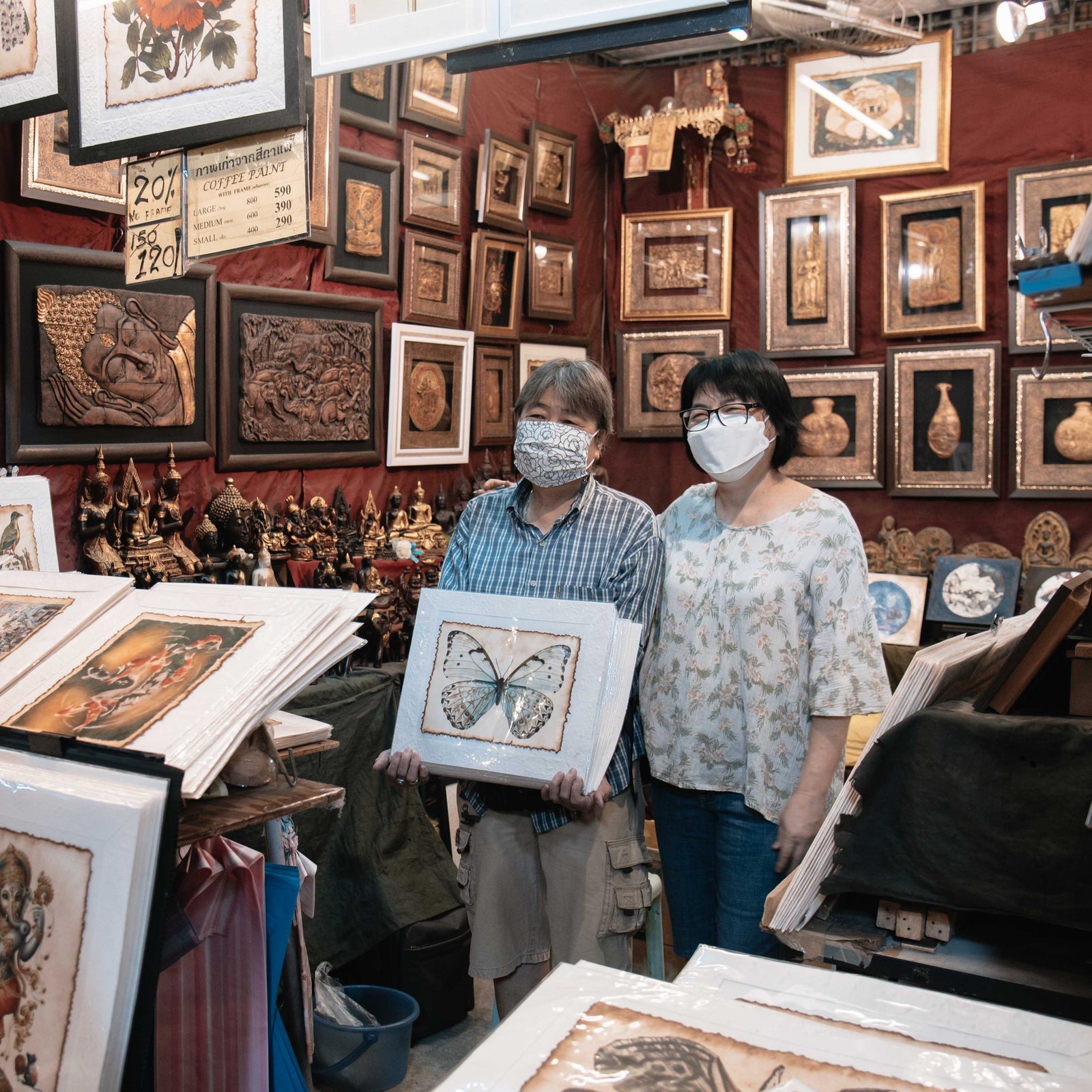 man and woman stand in shop of paper prints while holding a print of a butterfly made using coffee paper