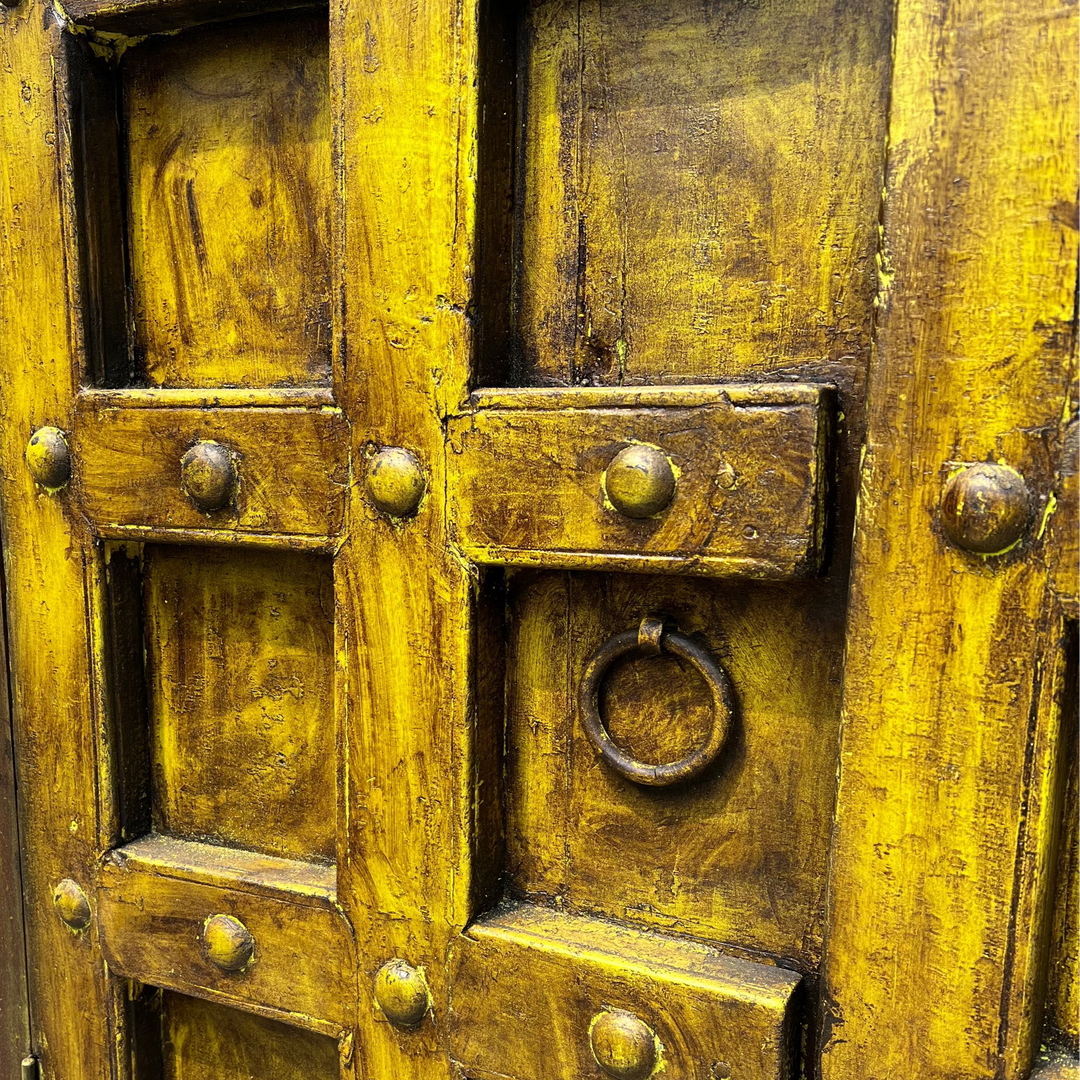 Close-up of a yellow rustic wooden door with metal accents and a circular handle.