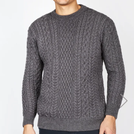 A male model wearing a gray, crew neck, 100% Merino wool Aran sweater with a traditional honeycomb stitch pattern.