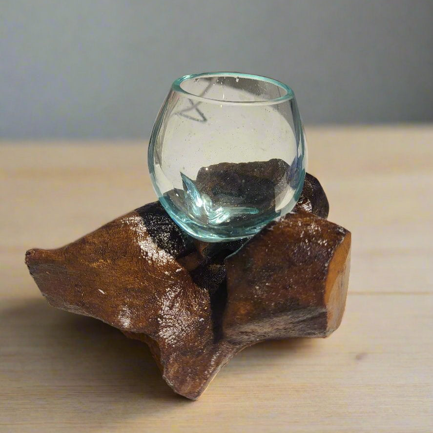 A mouth-blown glass globe on a natural wood base, with visible char marks on the wood.