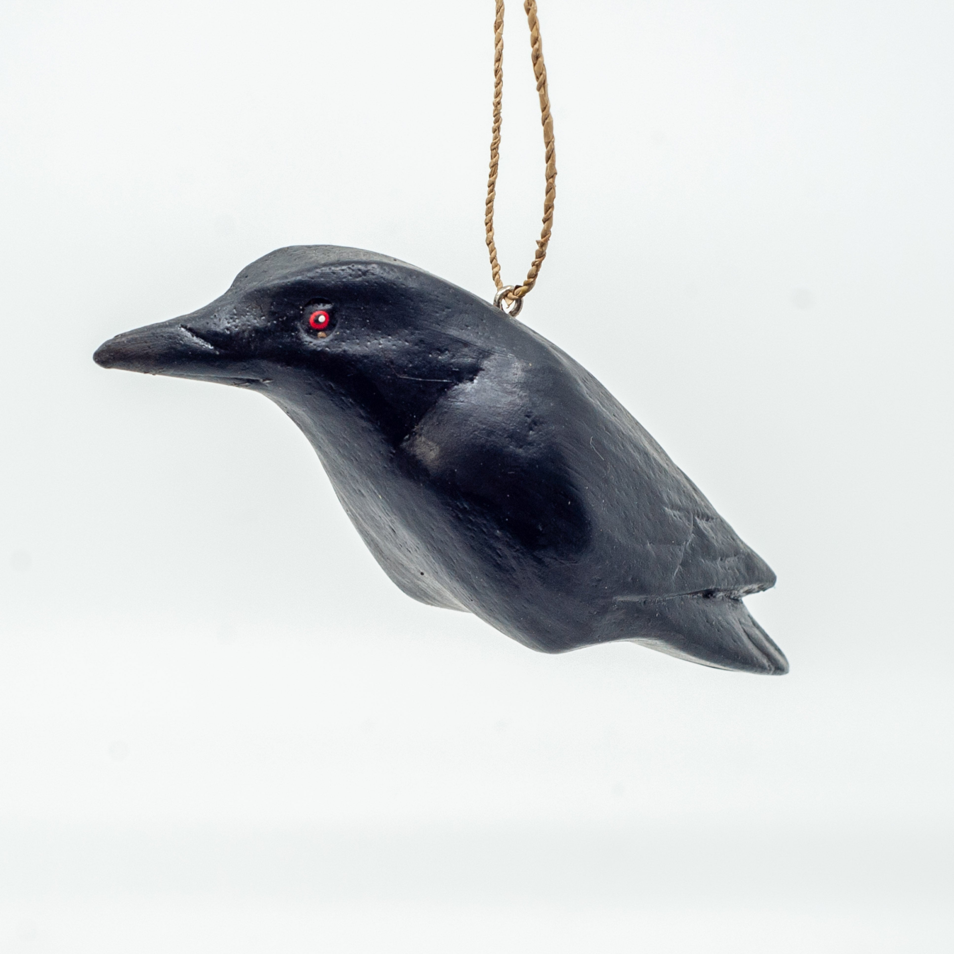 Small wooden crow ornament on white background hanging from string.