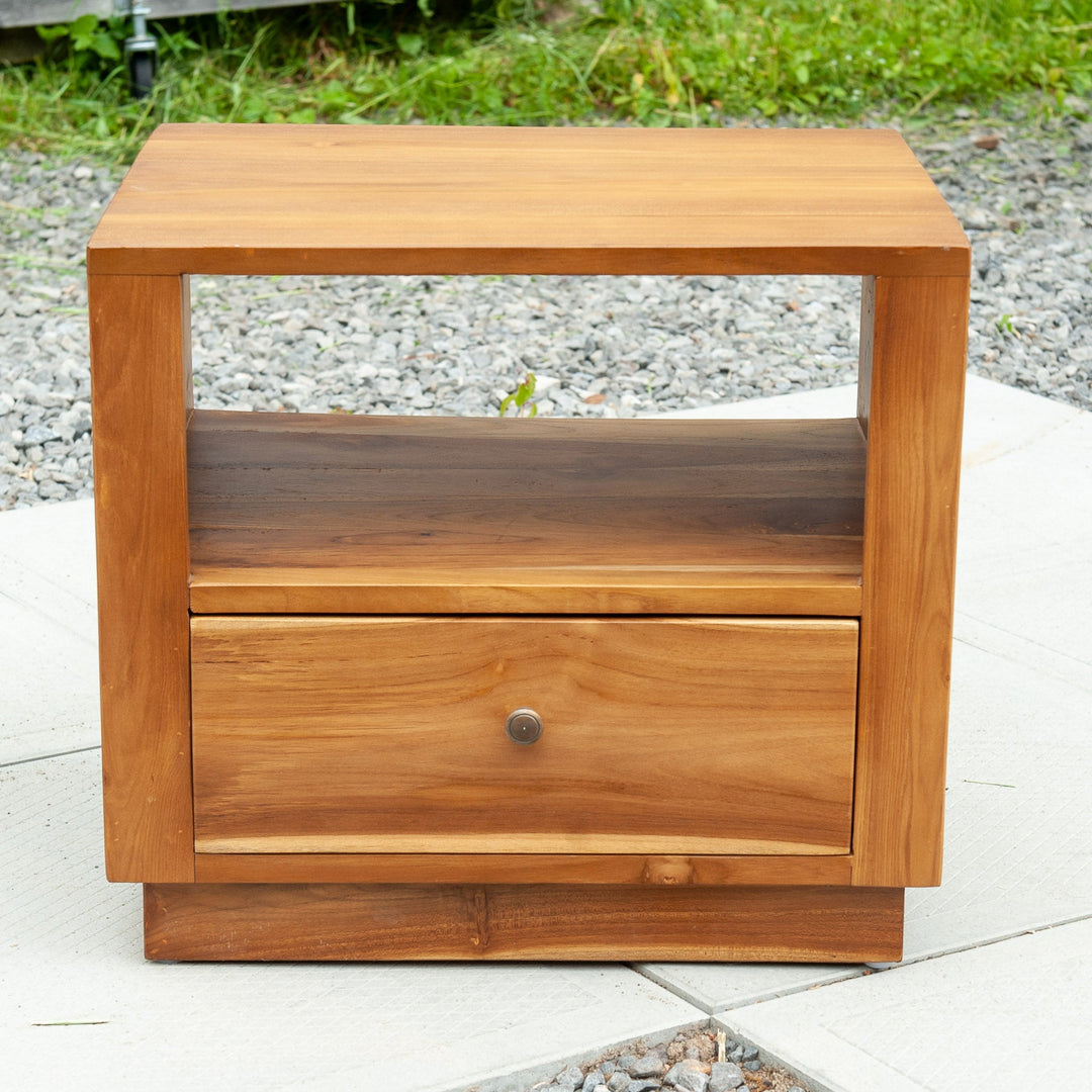 An image of a Java Teak Bedside Table. This beautifully crafted bedside table showcases the elegance and natural charm of Java teak wood. The table features a compact design, perfect for placing next to a bed. The rich, warm tones of the teak wood create a cozy and inviting atmosphere.
