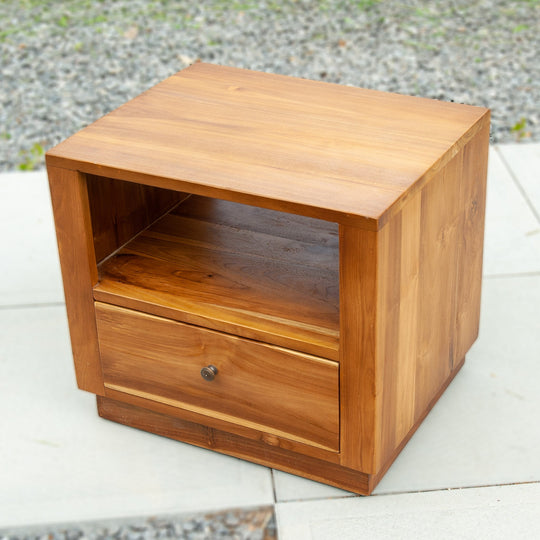 An image of a Java Teak Bedside Table. This beautifully crafted bedside table showcases the elegance and natural charm of Java teak wood. The table features a compact design, perfect for placing next to a bed. The rich, warm tones of the teak wood create a cozy and inviting atmosphere.