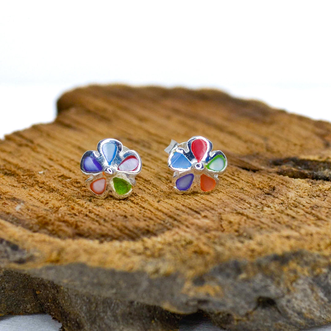 Rainbow coloured silver flower stud earrings on a piece of wood