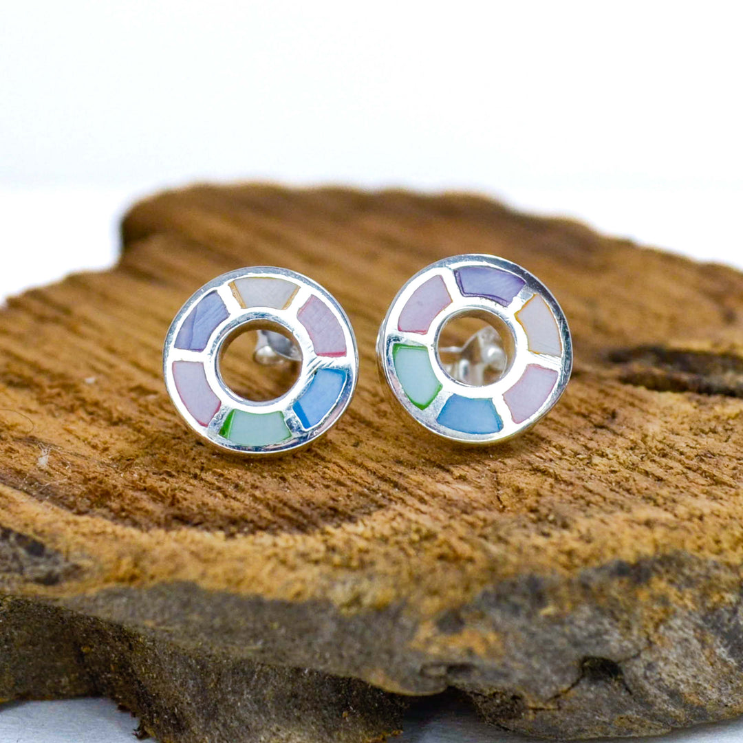Rainbow coloured silver circle pattern stud earrings on a piece of wood
