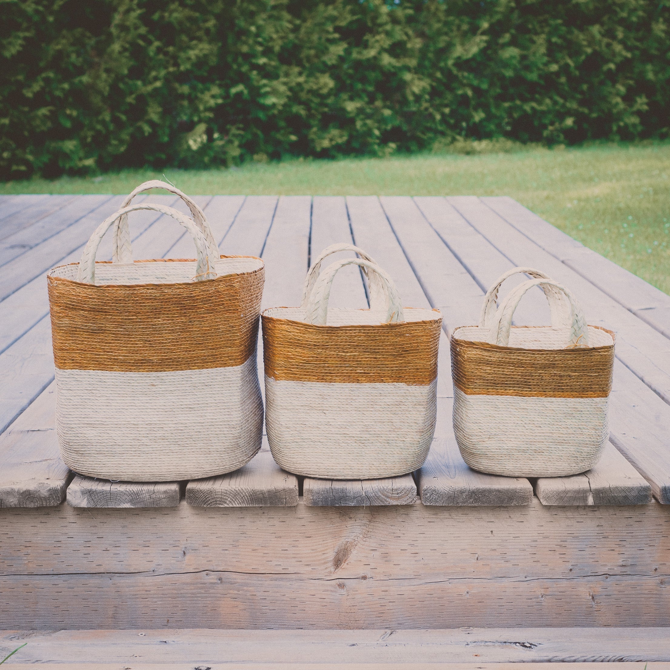 Natural woven baskets, three sizes on a wooden deck