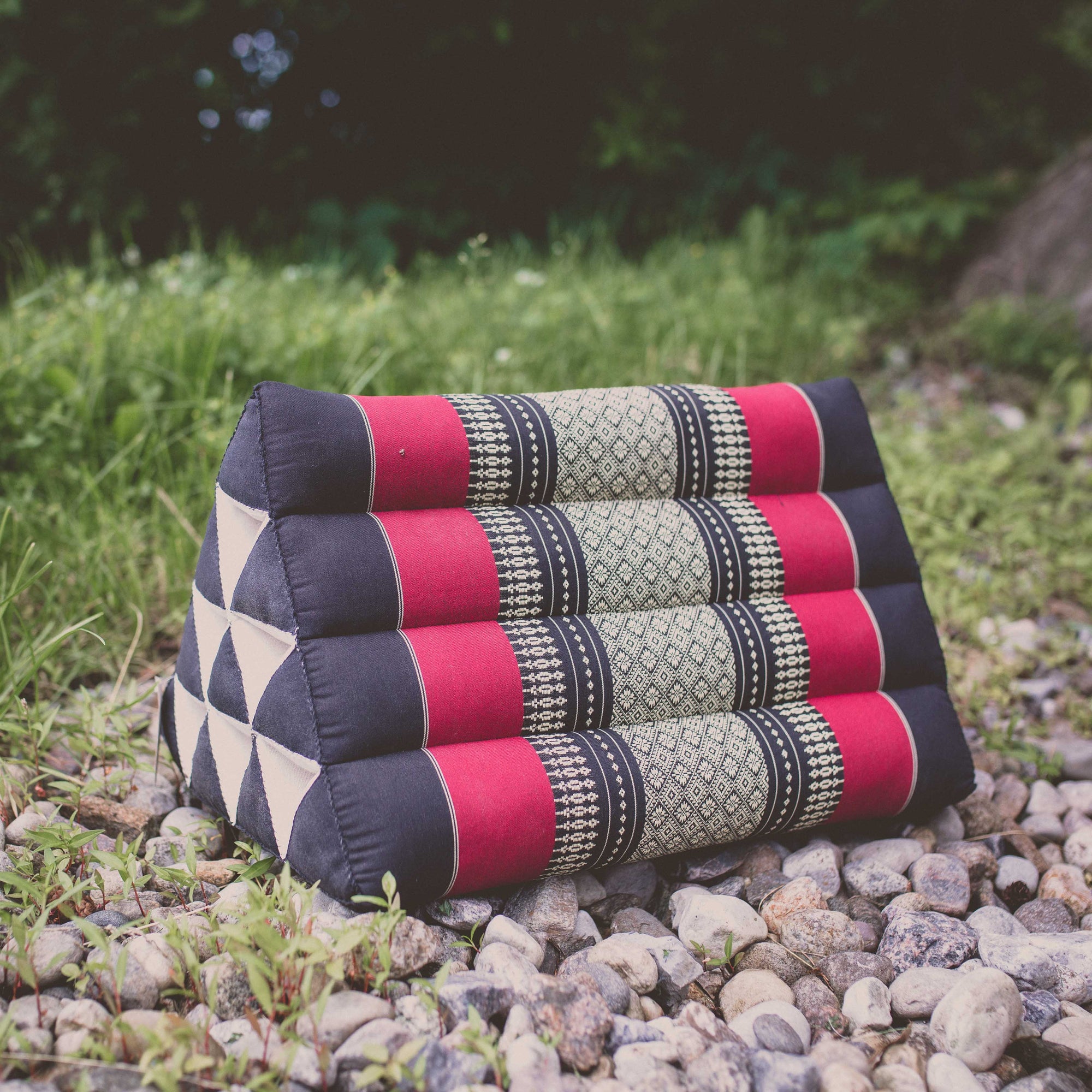 Photo of a triangular yoga support cushion with a deck or grassy background 