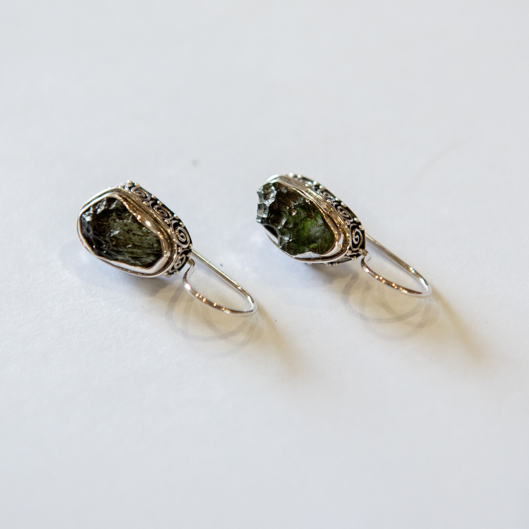 a pair of intricate, silver earrings with green stone on a white background
