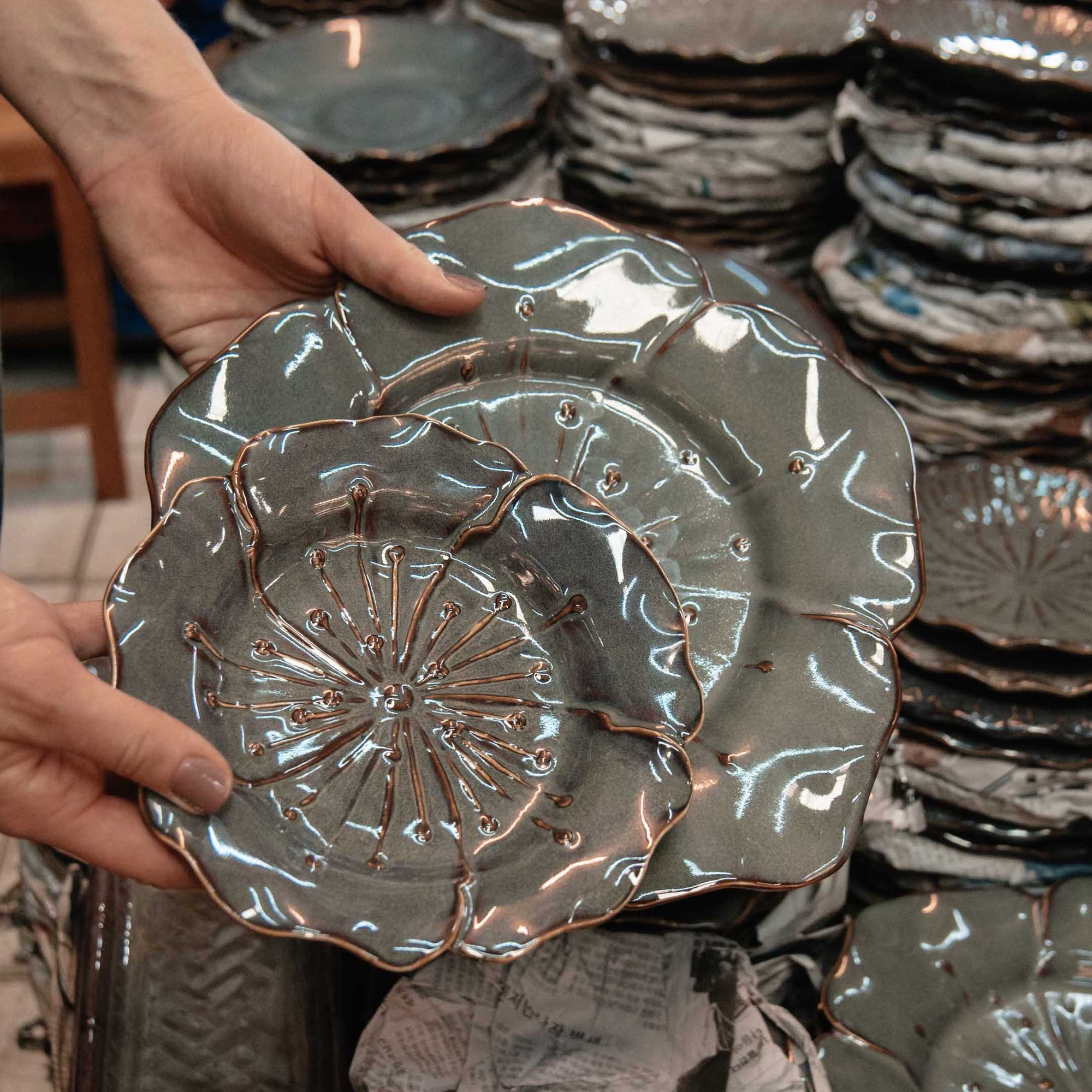 Hands holding up teal ceramic plates with designs on them