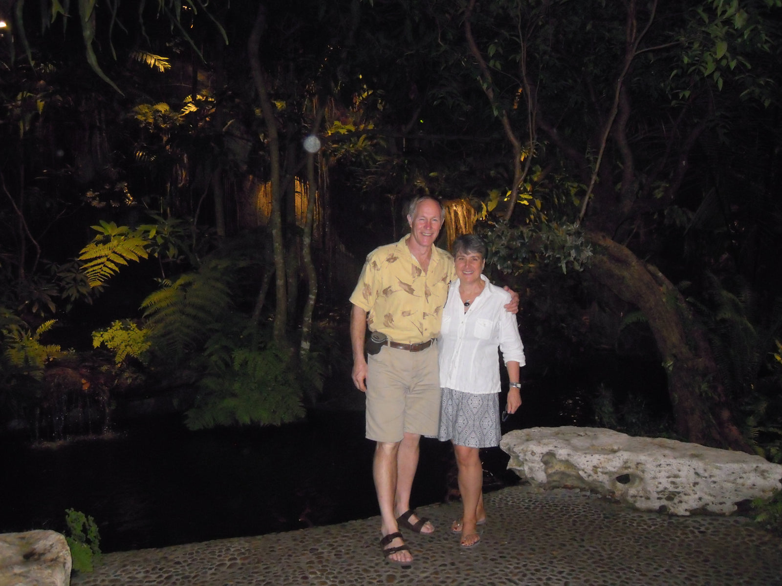 A man and woman standing in front of a dark jungle background in an open air 