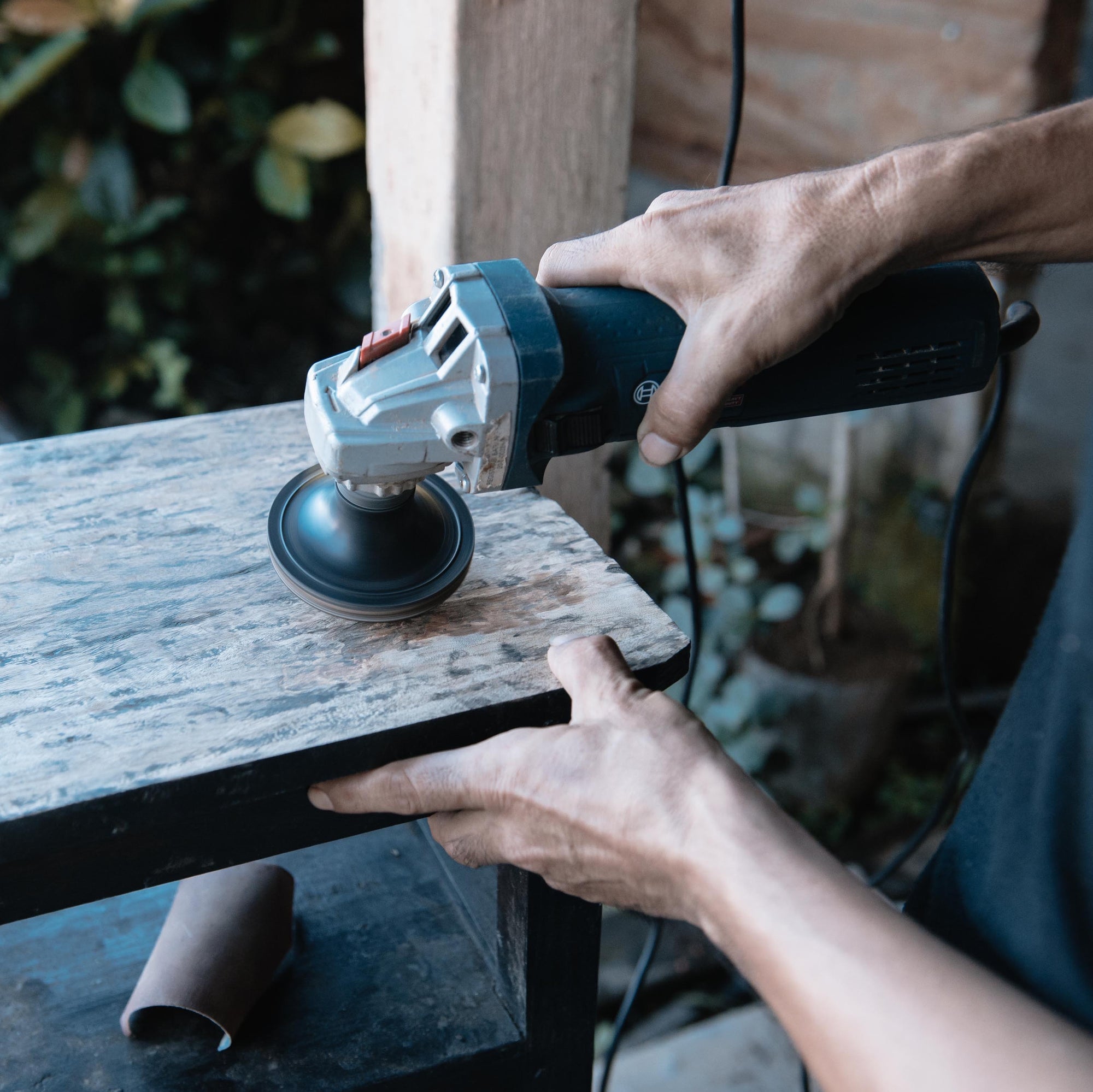 man sanding a piece of furniture with an electric sander outdoors 