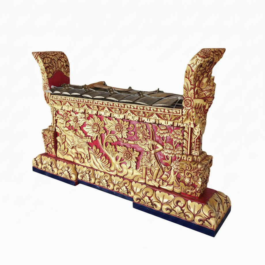 An authentic Balinese gamelan with bronze keys and a red lacquer finish, adorned with gold leaf embellishments and intricate carvings, placed on a wooden surface with a lush green background.