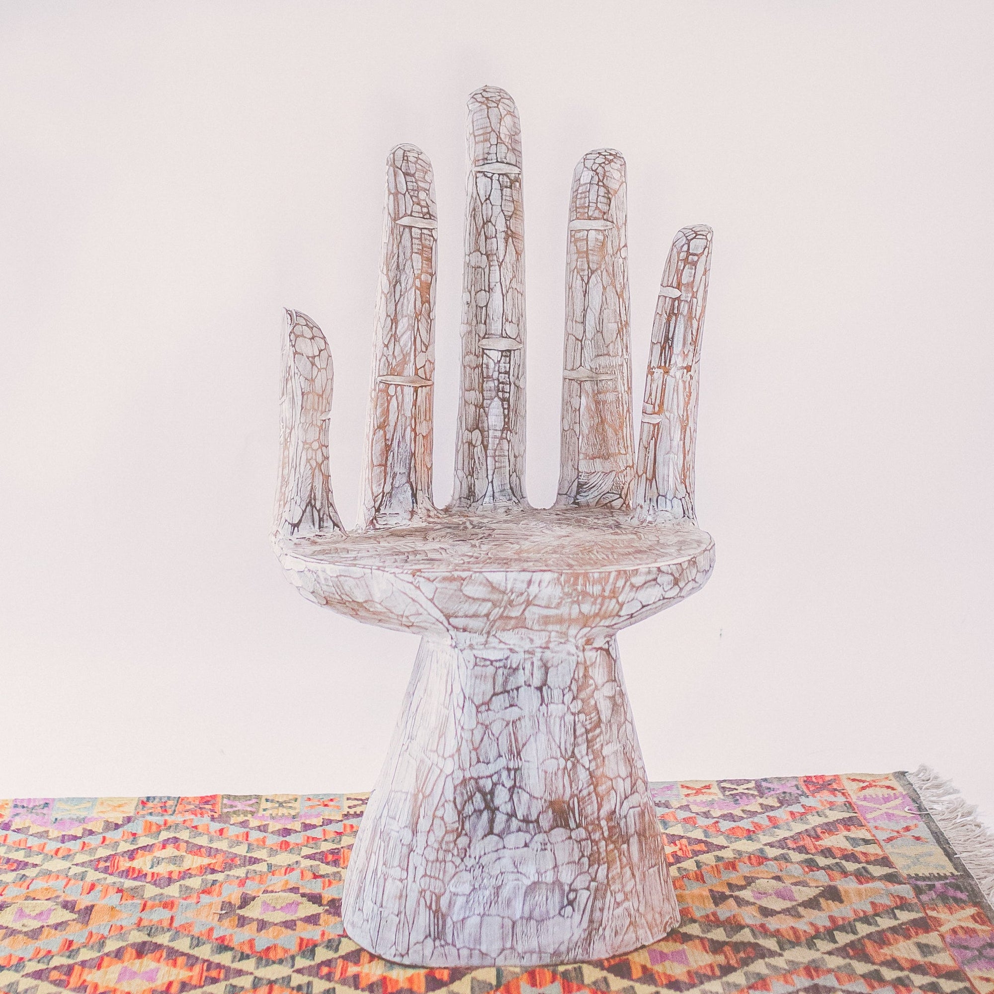 An image of an Indonesian Carved Hand-Shaped Chair. Carved from Indonesian wood, the chair is shaped like an intricately detailed hand, providing a one-of-a-kind design. The hand's fingers form the backrest and armrests, while the palm serves as the seat.  This chair is a captivating piece of functional art that combines creativity with functionality, making it a striking addition to any living space or artistic setting