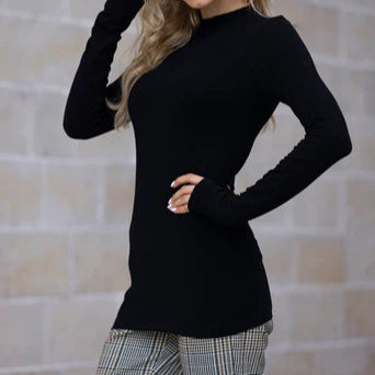 A woman wearing a black mock neck bamboo turtleneck top paired with patterned trousers.