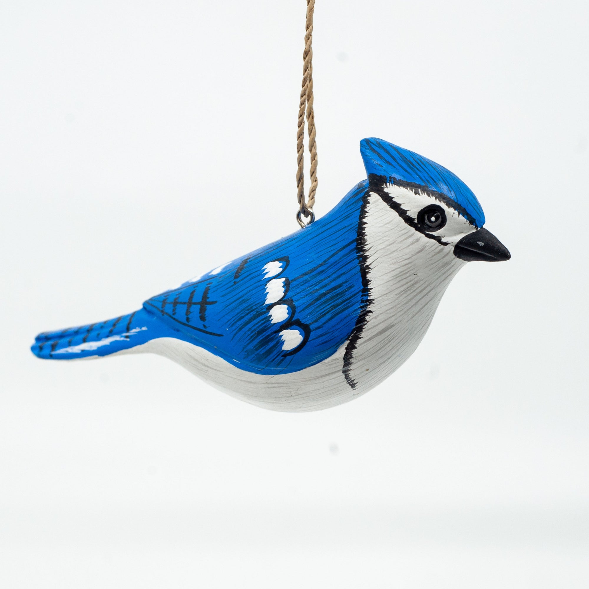 Small wooden bluejay ornament on white background hanging from string. 