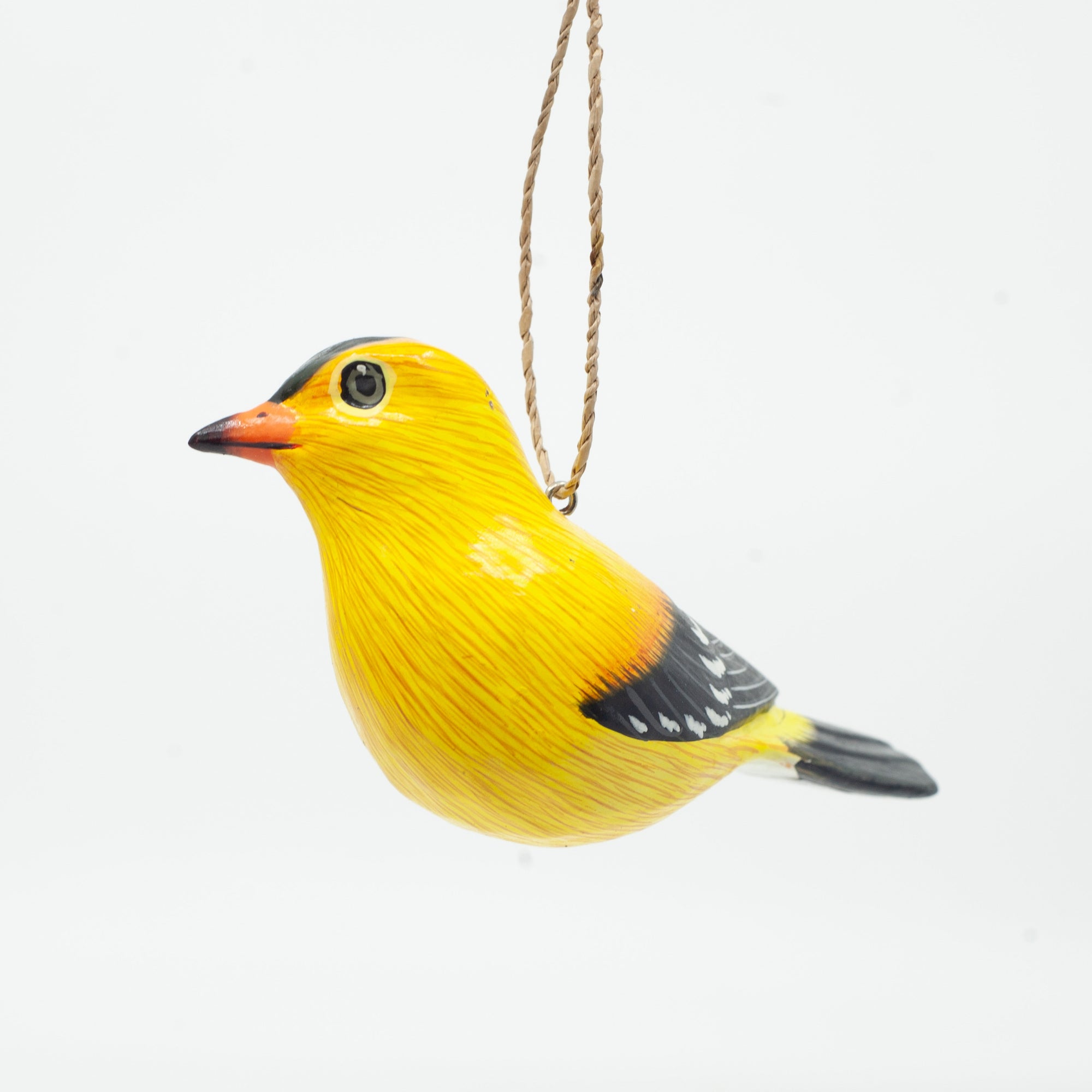 Small wooden goldfinch ornament on white background hanging from string. 
