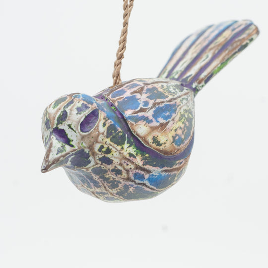 Small driftwood bird ornament on white background hanging from string. 