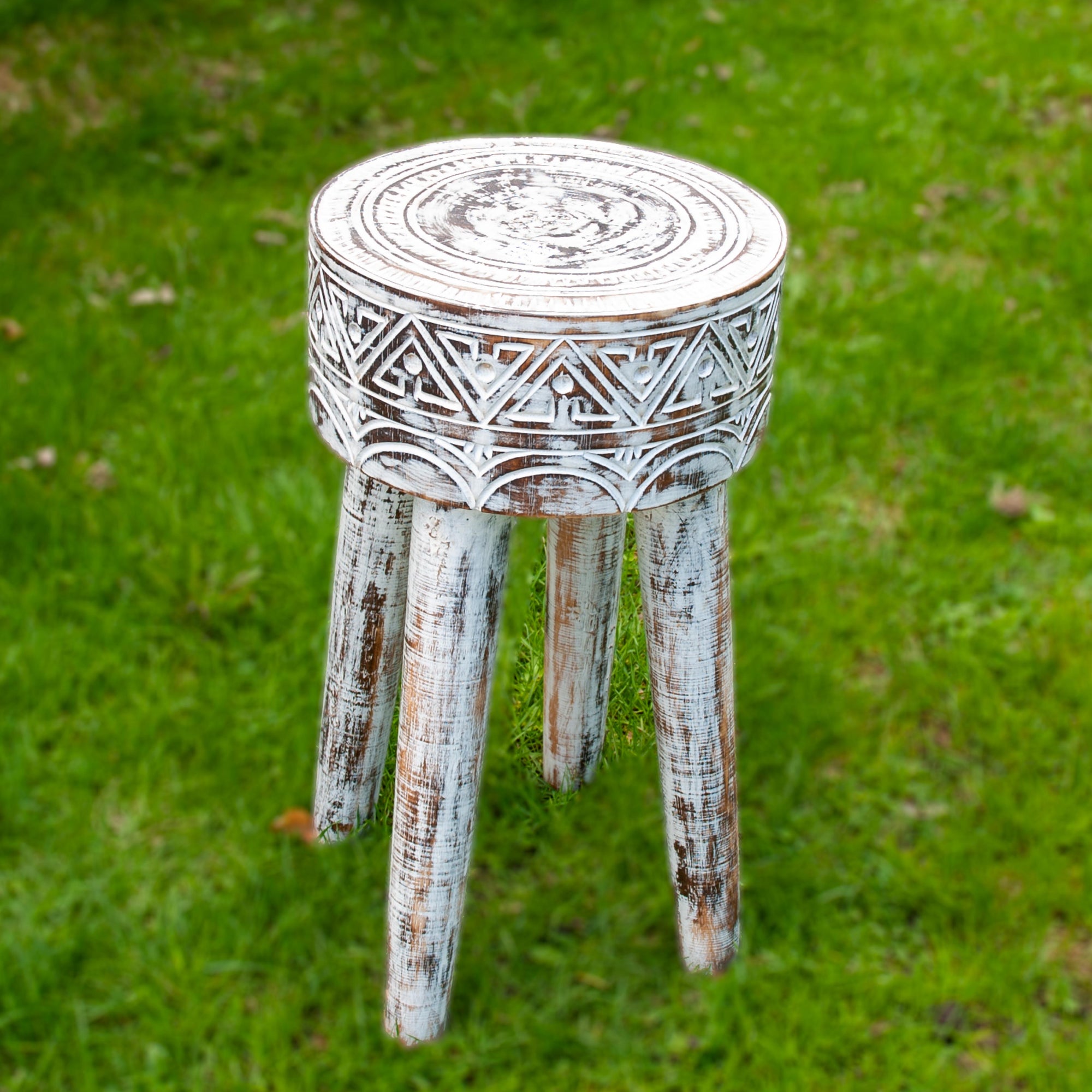 Small white three legged stool with tribal style carvings on grass