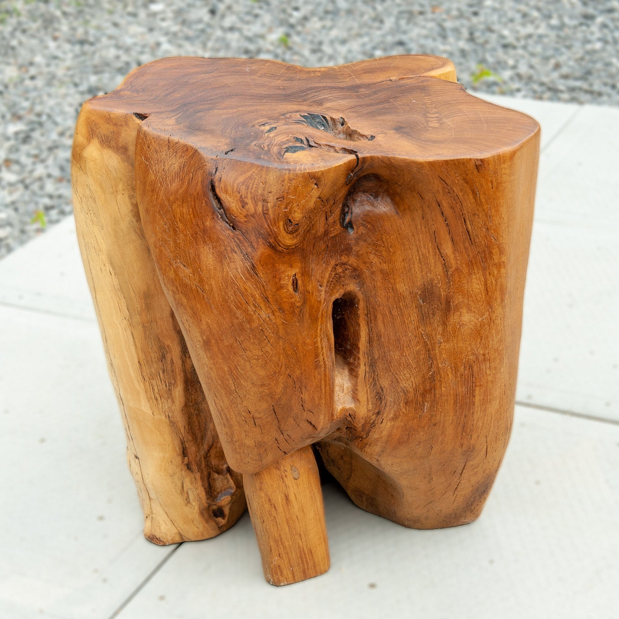 An image of a Teak Trunk Stool. This unique stool is crafted from a teak trunk, preserving the natural beauty and character of the wood. The stool showcases the rich textures, grains, and unique patterns found in teak. With its solid and sturdy construction, it serves as both a functional seating option and a piece of natural art.