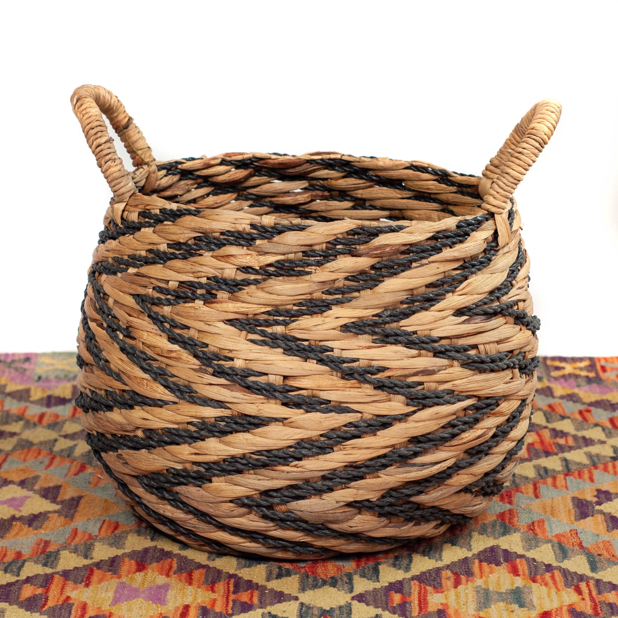 Woven basket made out of water hyacinth planter in natural tone with black accents and handles on neutral background