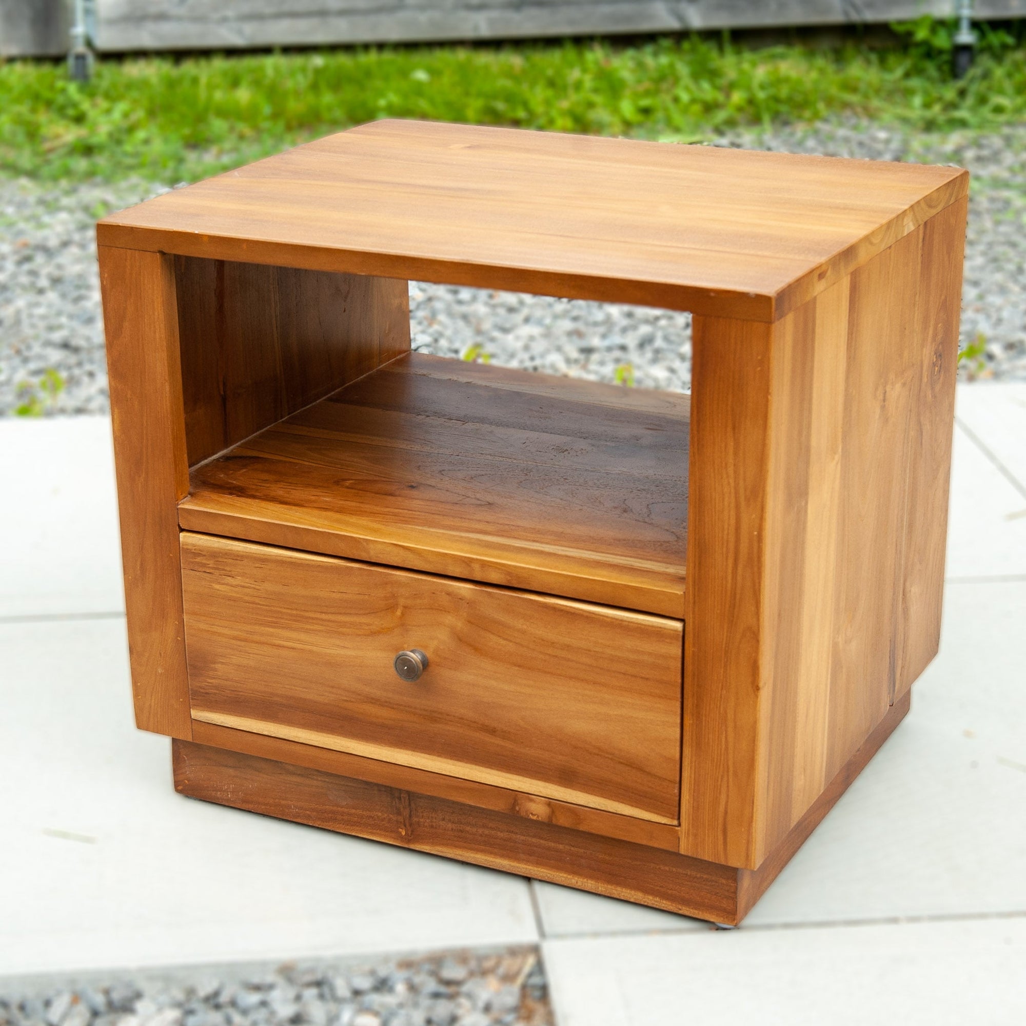 An image of a Java Teak Bedside Table. This beautifully crafted bedside table showcases the elegance and natural charm of Java teak wood. The table features a compact design, perfect for placing next to a bed. The rich, warm tones of the teak wood create a cozy and inviting atmosphere.