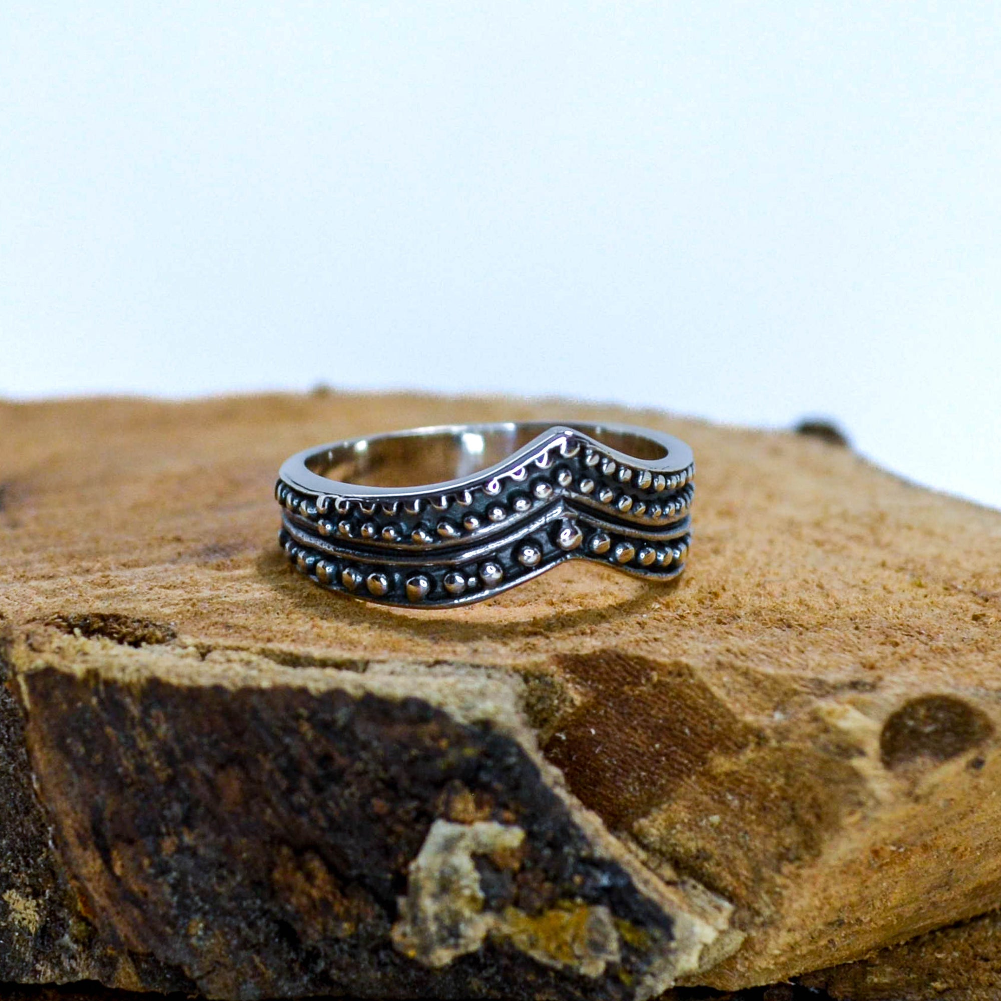 V shaped silver ring with dots sitting on wood