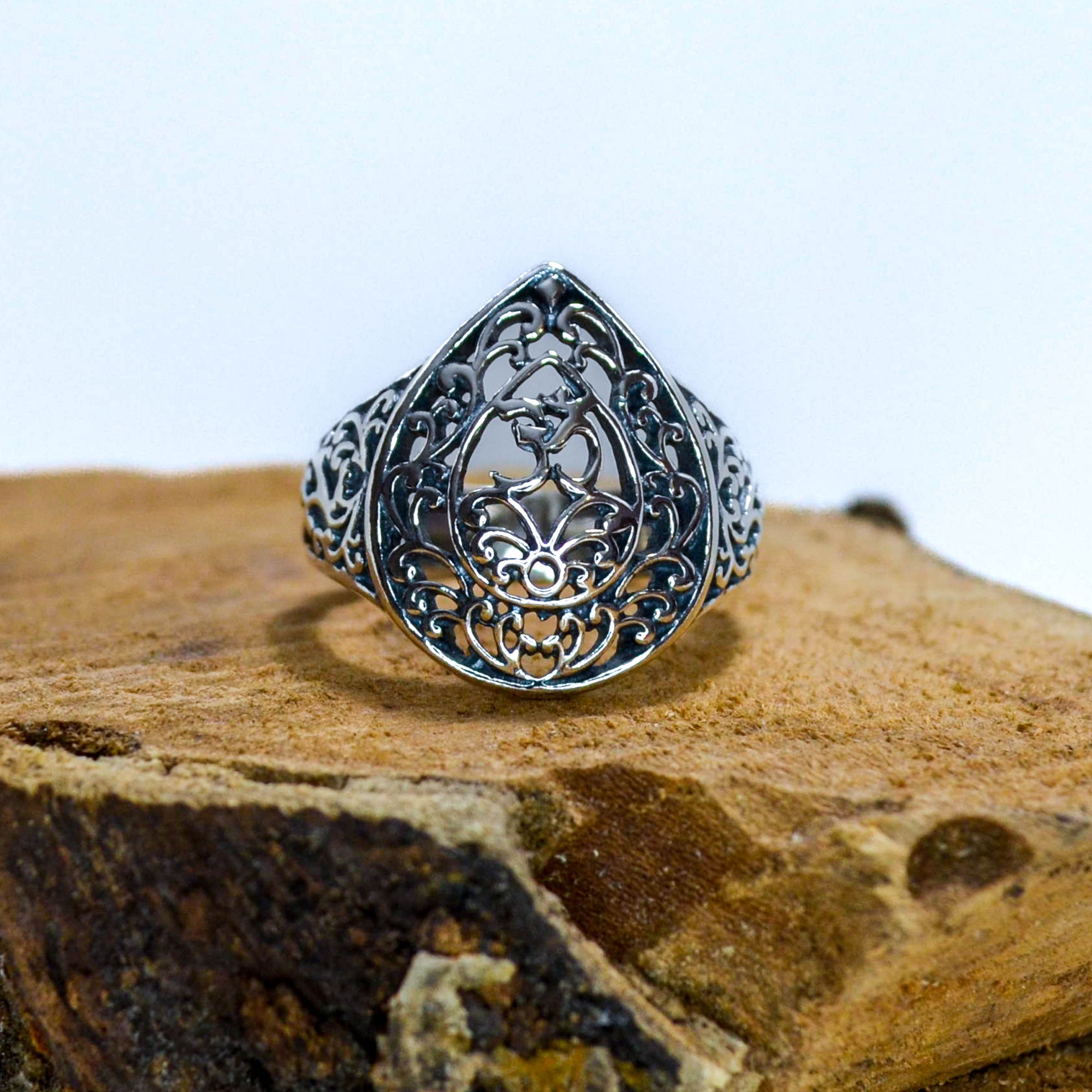 Ornate silver ring in a teardrop shape with small OM symbol sitting on wood