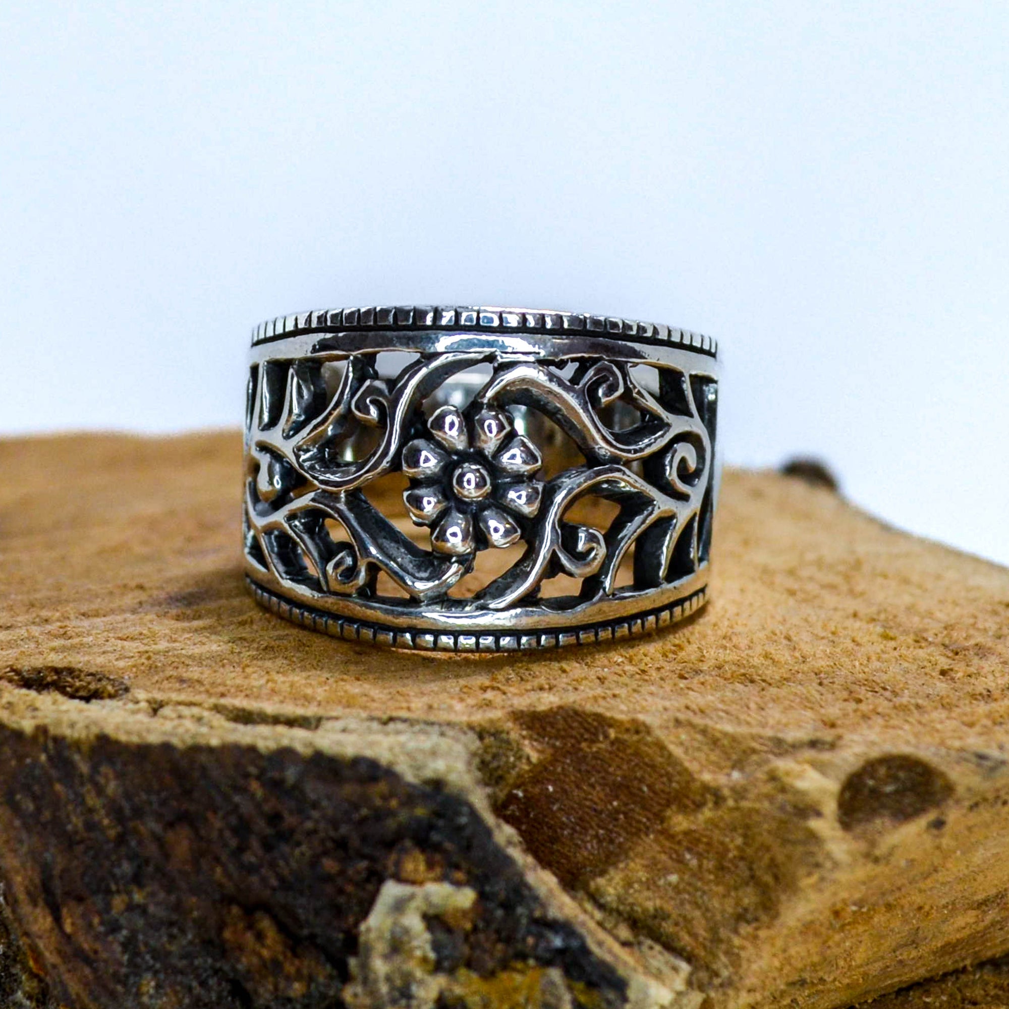 Ornate silver ring with a small flower in the center sitting on wood