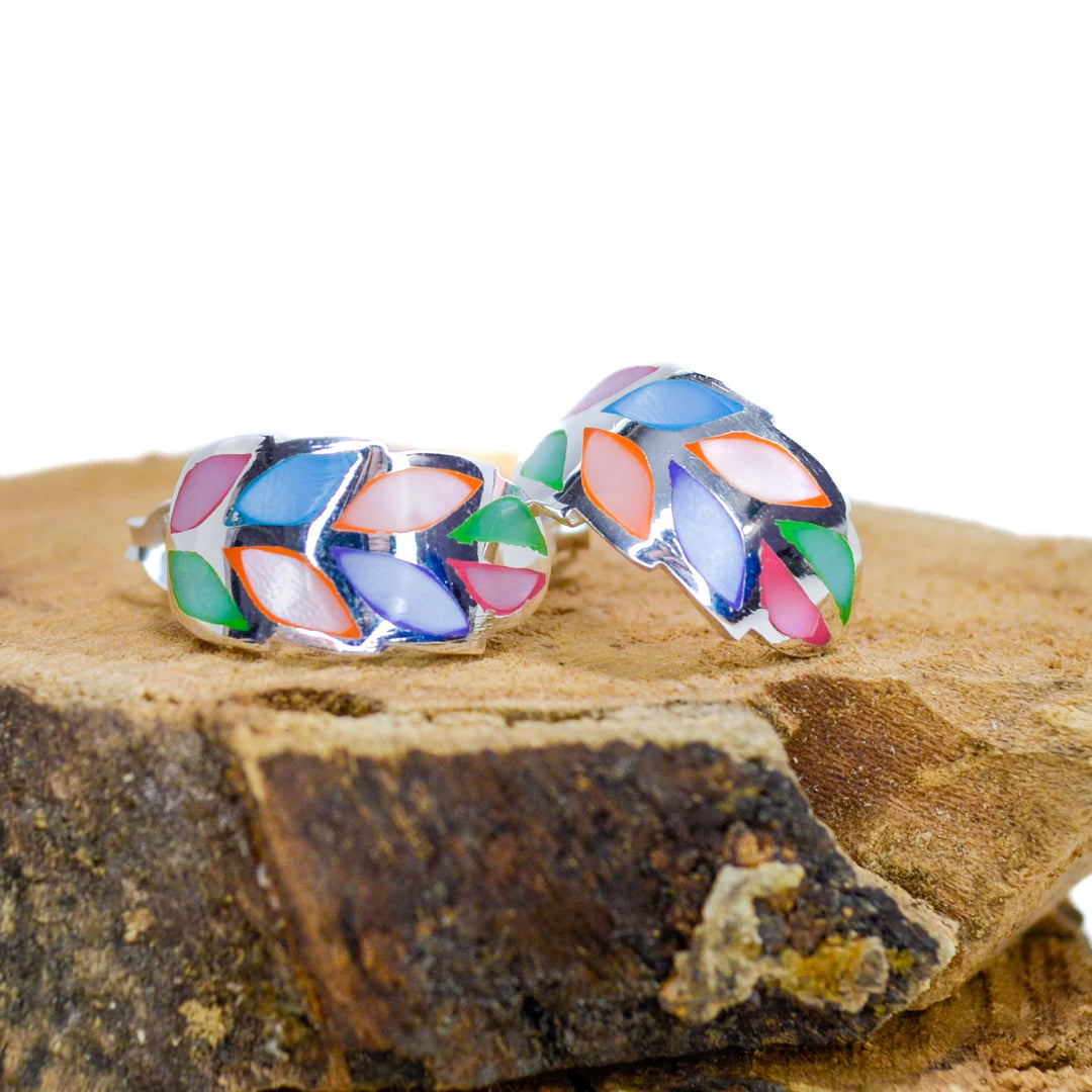 Rainbow coloured silver leaf stud earrings on a piece of wood