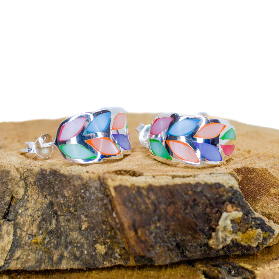 Rainbow coloured silver leaf stud earrings on a piece of wood