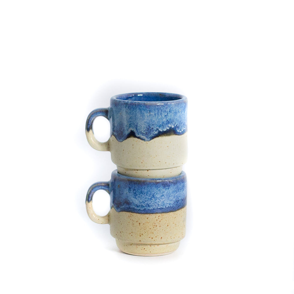 Small blue and cream coffee mugs stacked on white background